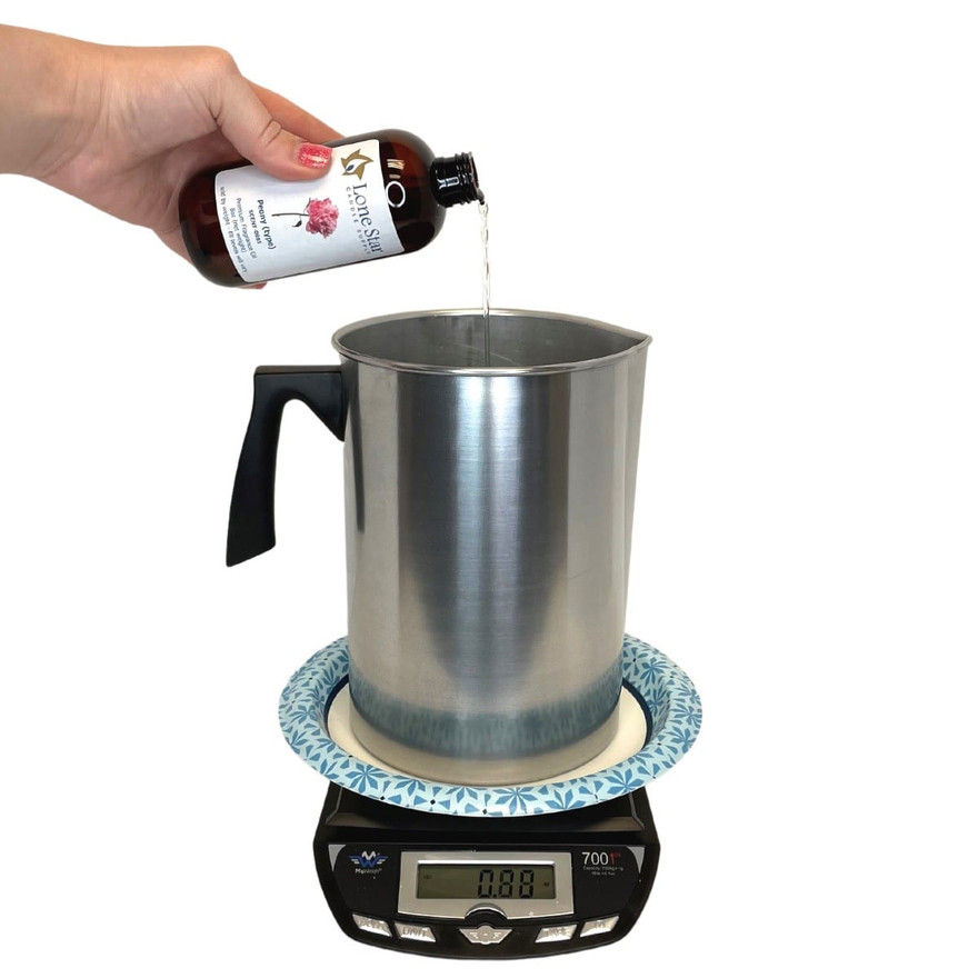 Hand pouring Lone Star Peony fragrance oil from an amber bottle into a pouring pot on a digital scale
