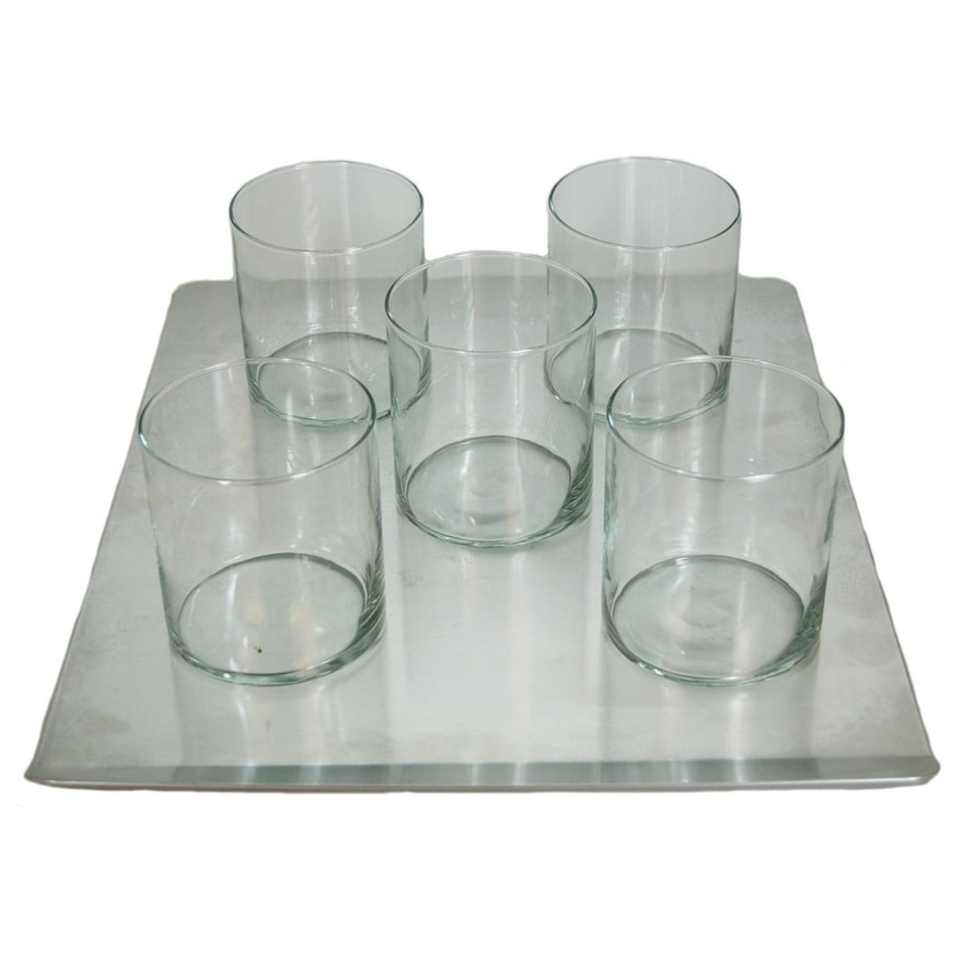 Five empty clear glass candle tumblers arranged on a square metal tray