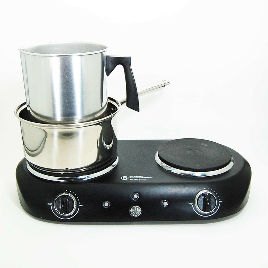 Aluminum pouring pitcher set in a saucepan of water on a black double-burner hot plate