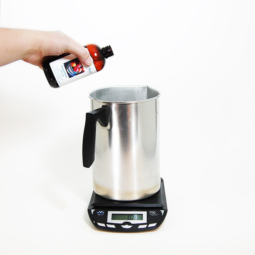 Hand tipping an amber Lone Star fragrance oil bottle over a metal pitcher on a digital scale