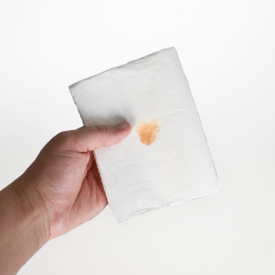 Hand holding a white paper towel showing a small orange wax color-test smear