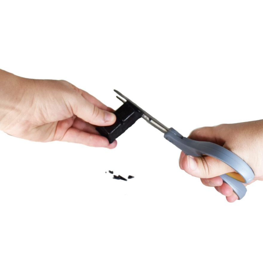 Hands shaving a piece off a black dye block with scissors over scattered dye flakes
