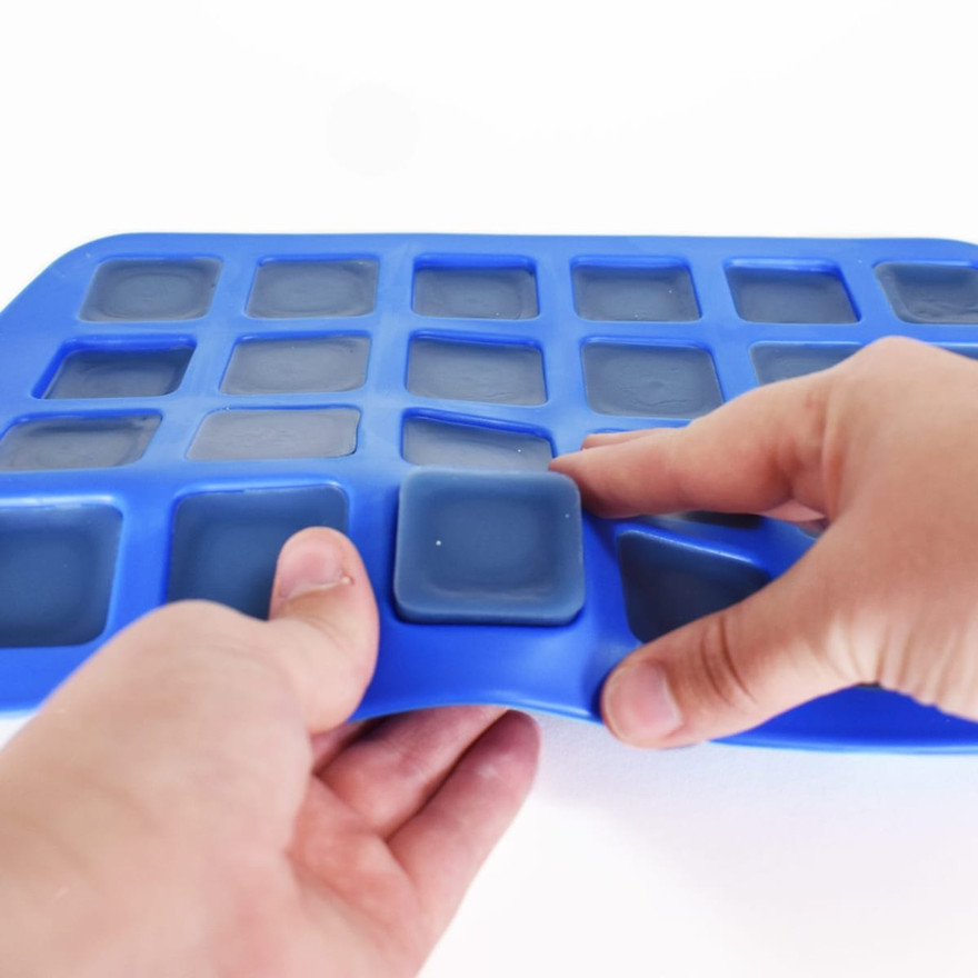 Hands flexing a blue silicone mold to pop out a finished square wax tart