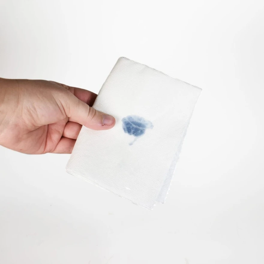 Hand holding a folded white paper towel marked with a small blue wax color test