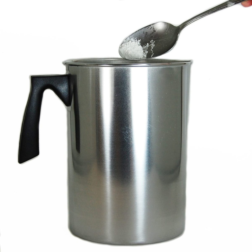 Spoonful of white powder additive held over the rim of a metal pouring pitcher